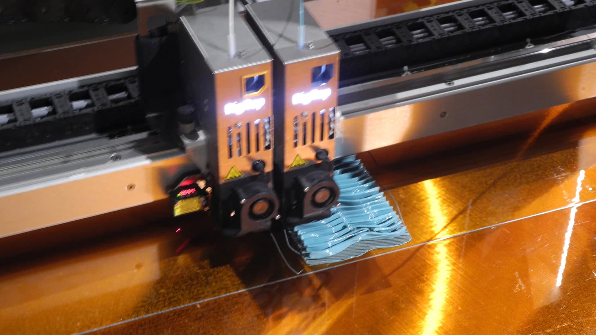 Close-up of a 3D printer head laying blue plastic onto a build plate
